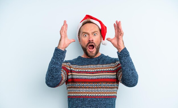 Middle age handsome man screaming with hands up in the air. christmas concept