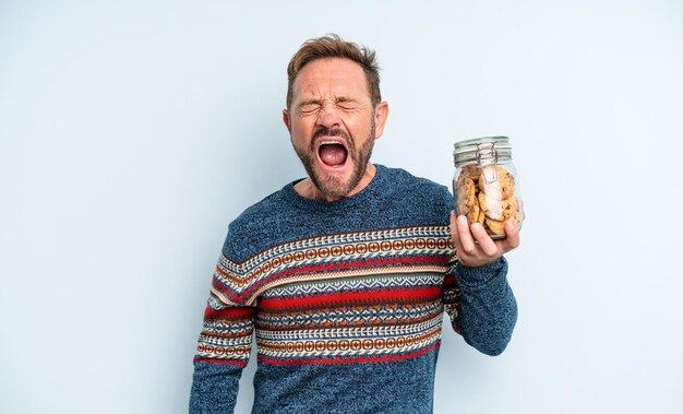 Middle age handsome man shouting aggressively, looking very angry. cookies bottle