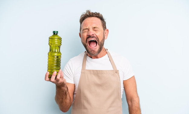 Middle age handsome man shouting aggressively, looking very angry. olive oil concept