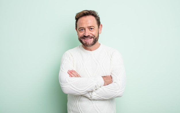 Middle age handsome man smiling to camera with crossed arms and a happy, confident, satisfied expression, lateral view