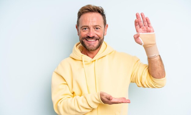 Middle age handsome man smiling cheerfully feeling happy and showing a concept broken hand concept