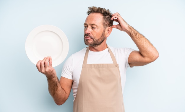 Middle age handsome man smiling happily and daydreaming or doubting. empty dish concept