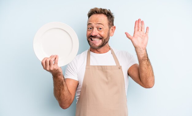 Foto uomo bello di mezza età che sorride felicemente, agitando la mano, accogliendoti e salutandoti. concetto di piatto vuoto