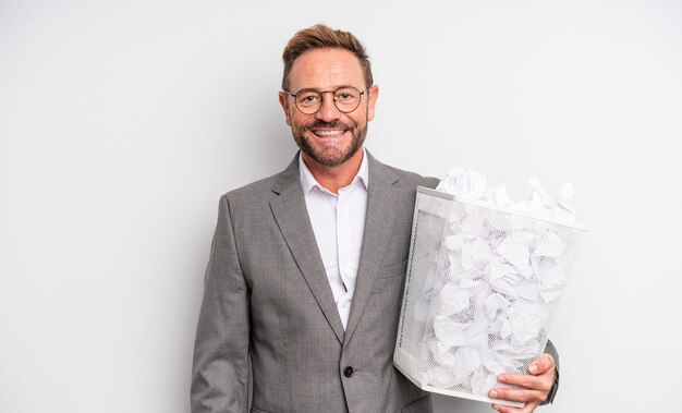 Middle age handsome man smiling happily with a hand on hip and confident paper balls trash concept