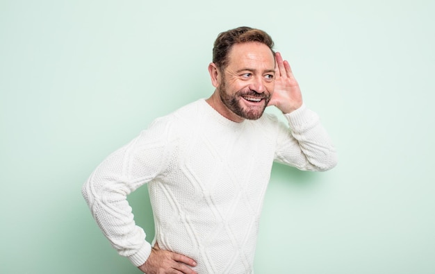 Middle age handsome man smiling looking curiously to the side trying to listen to gossip or overhearing a secret