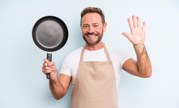 Middle age handsome man smiling and looking friendly, showing number five. frying pan concept