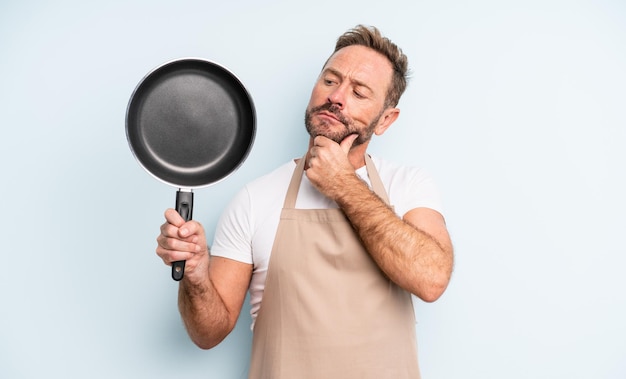 Middle age handsome man thinking, feeling doubtful and confused. frying pan concept