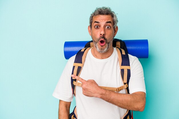 Middle age hiker caucasian man isolated on blue background  pointing to the side