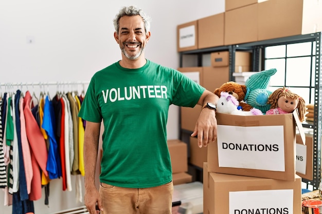 寄付スタンドでボランティアのTシャツを着た中年のヒスパニック系男性が、幸せでクールな笑顔を浮かべています。幸運な人。