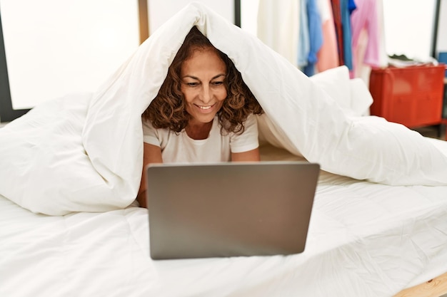 Middle age hispanic woman smiling confident using laptop at bedroom