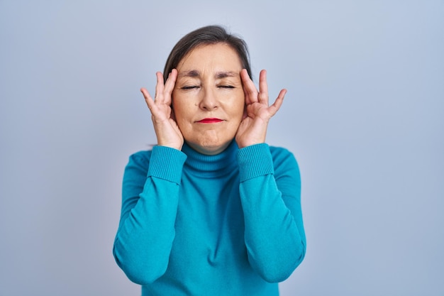 Middle age hispanic woman standing over isolated background with hand on head for pain in head because stress. suffering migraine.