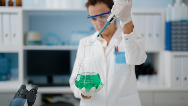 Foto donna ispanica di mezza età che indossa l'uniforme da scienziato che lavora in laboratorio