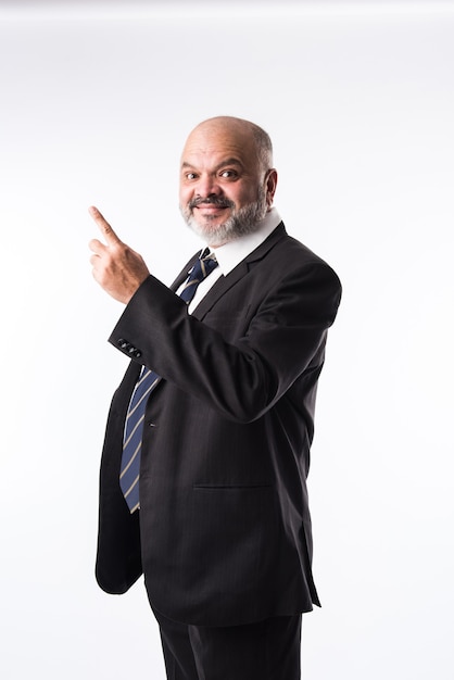 Middle age Indian asian businessman with beard wearing elegant black suit and pointing with hand and finger. presenting product, service or copy space