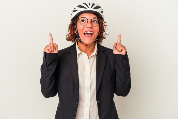 Middle age latin business woman wearing a bike helmet isolated on white background pointing upside with opened mouth.