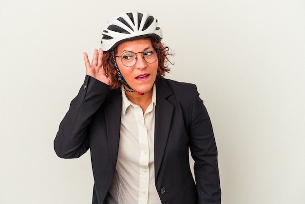 Middle age latin business woman wearing a bike helmet isolated on white background trying to listening a gossip.