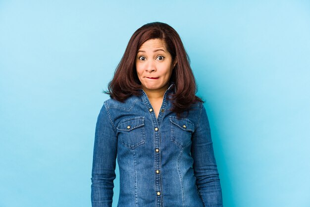 Middle age latin woman on a blue background confused, feels doubtful and unsure.