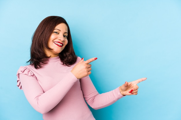 Middle age latin woman excited pointing with forefingers away.