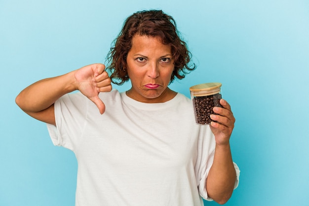 Middle age latin woman holding a coffee jar isolated on blue background showing a dislike gesture, thumbs down. Disagreement concept.