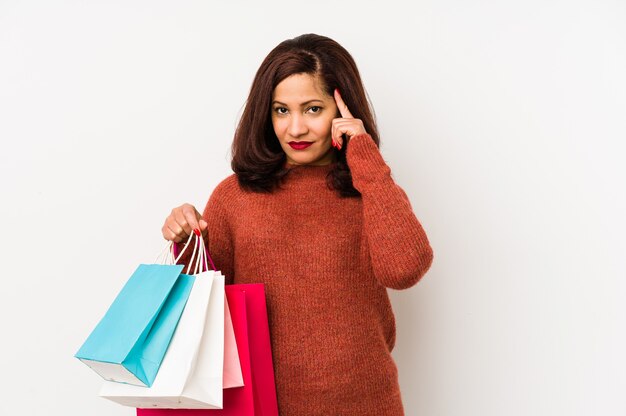 Middle age latin woman holding a shopping bags isolated pointing temple with finger, thinking, focused on a task.