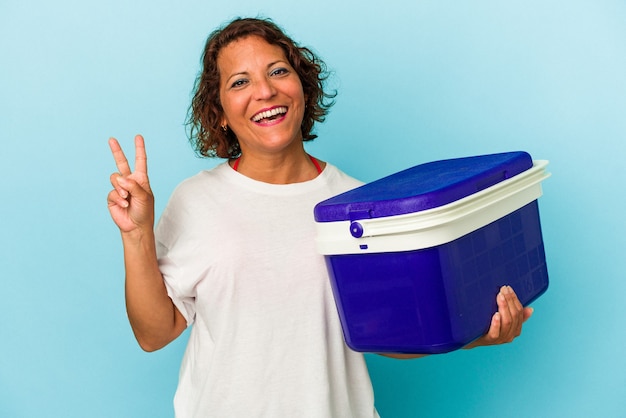 Middle age latin woman isolated on blue background joyful and carefree showing a peace symbol with fingers.