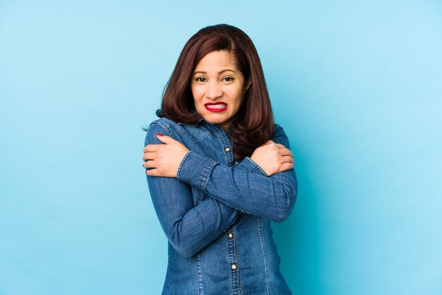 Middle age latin woman isolated on a blue wall going cold due to low temperature or a sickness.