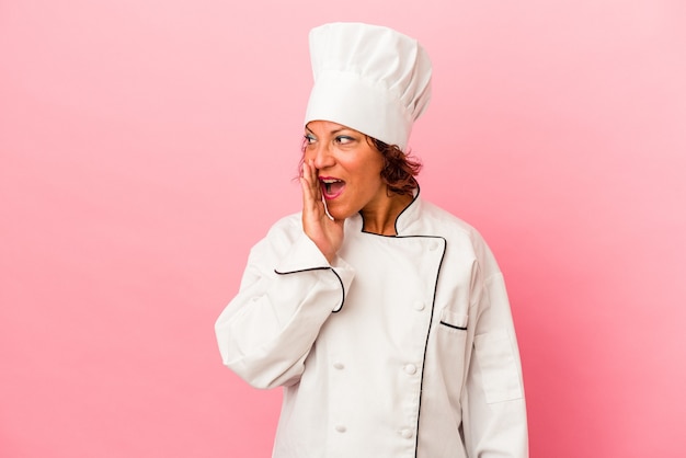 Middle age latin woman isolated on pink background is saying a secret hot braking news and looking aside