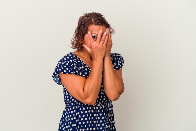 Photo middle age latin woman isolated on white background blink through fingers frightened and nervous.