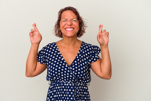 Middle age latin woman isolated on white background crossing fingers for having luck