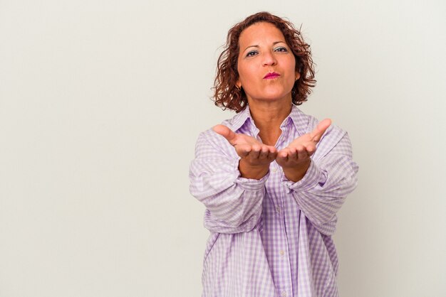 Middle age latin woman isolated on white background folding lips and holding palms to send air kiss.