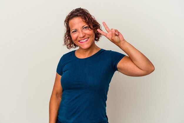 Middle age latin woman isolated on white background joyful and carefree showing a peace symbol with fingers.