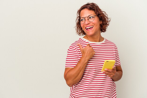 Middle age latin woman isolated on white background points with thumb finger away, laughing and carefree.