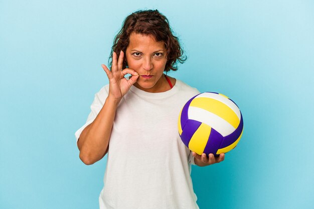 Middle age latin woman playing volleyball isolated on blue background with fingers on lips keeping a secret.