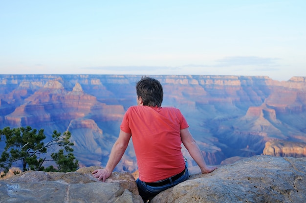 Middle age male tourist sitting on stone and looking of the Grand Canyon from Mather Point