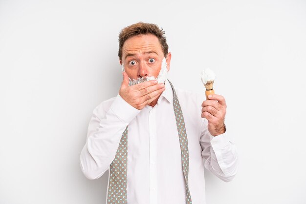 Middle age man covering mouth with hands with a shocked. shaving brush and foam concept