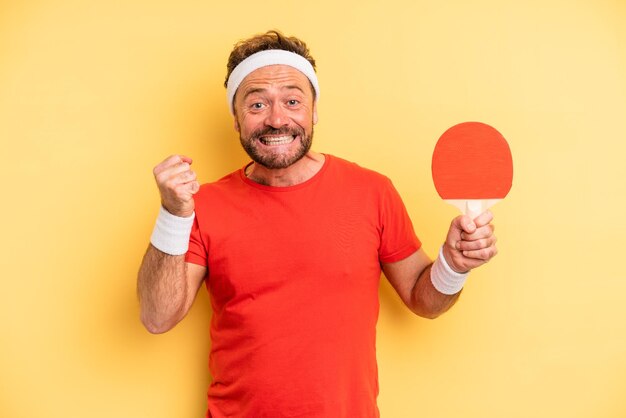 Photo middle age man feeling shocked,laughing and celebrating success. ping pong concept