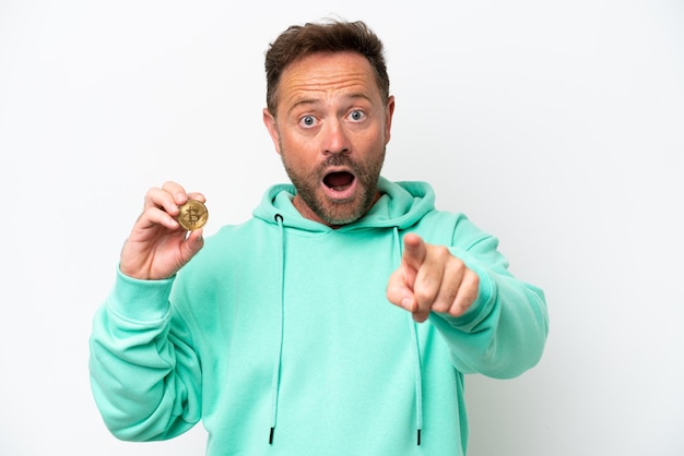 Photo middle age man holding a bitcoin over isolated background surprised and pointing front