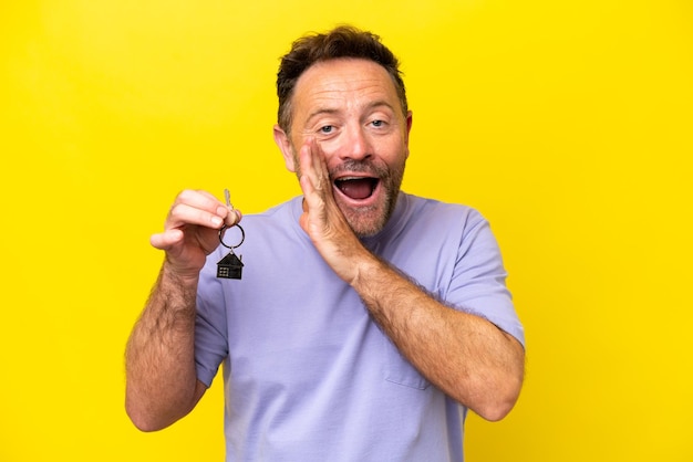 Middle age man holding home keys isolated on yellow background whispering something