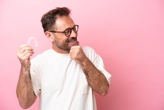 Middle age man holding invisible braces isolated on pink background thinking an idea and looking side