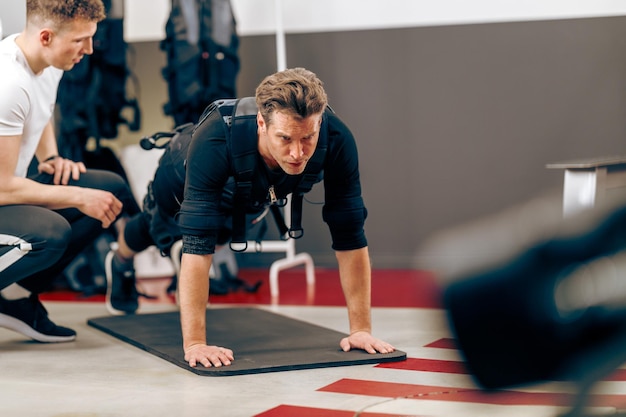 L'uomo di mezza età sta facendo esercizi di plancia durante l'allenamento ems con l'allenatore in palestra.