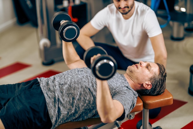 Middle age man is doing training with personal trainer in a gym.