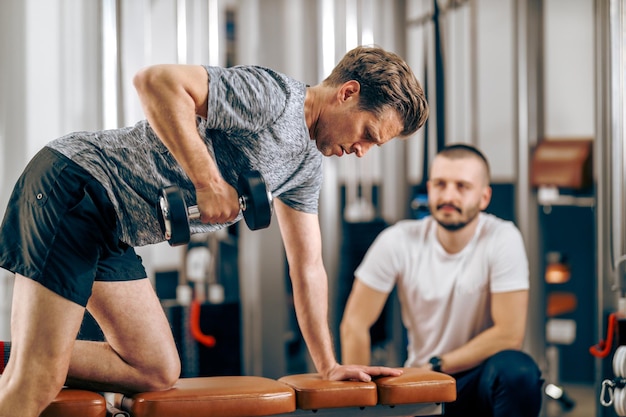 Middle age man is doing training with personal trainer in a gym.