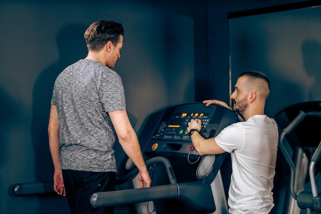 Middle age man is exercising on a treadmill with coach in the gym.