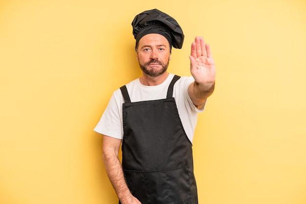 Middle age man looking serious showing open palm making stop gesture. chef concept