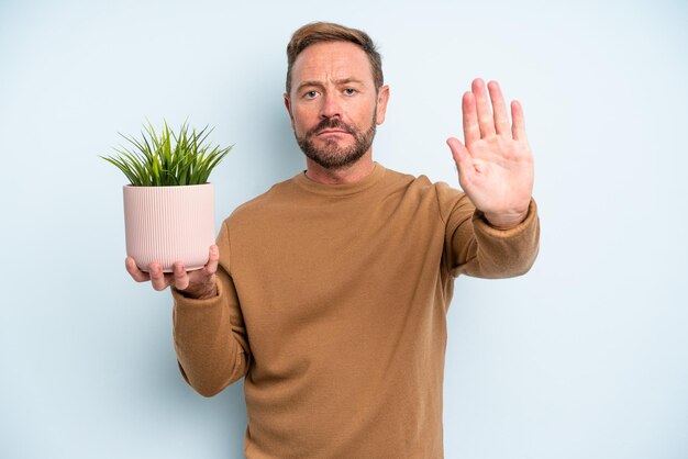 Middle age man looking serious showing open palm making stop gesture plant pot concept