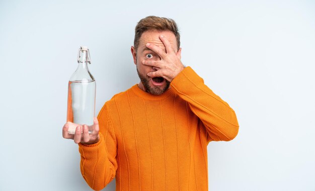 Uomo di mezza età che sembra scioccato, spaventato o terrorizzato, coprendo il viso con la mano. concetto di bottiglia d'acqua