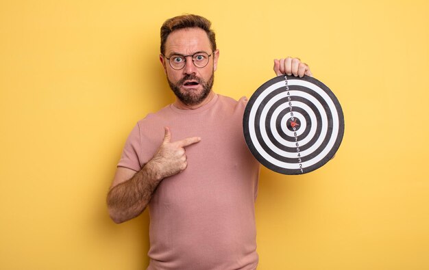 Middle age man looking shocked and surprised with mouth wide open, pointing to self. dart diana concept