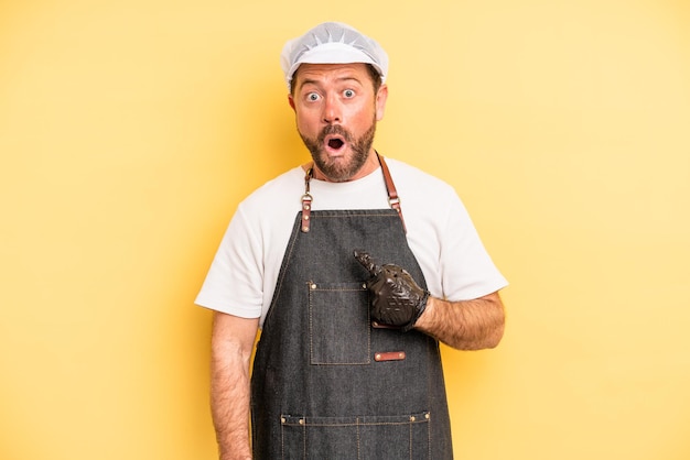 Middle age man looking shocked and surprised with mouth wide open, pointing to self. fishmonger concept