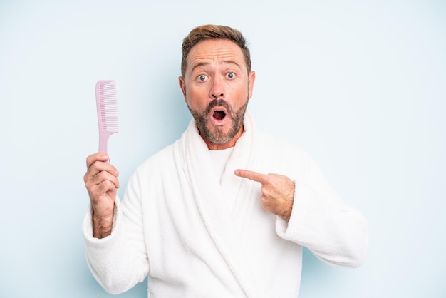 Middle age man looking shocked and surprised with mouth wide open, pointing to self. hair comb concept