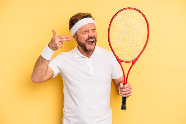 Middle age man looking unhappy and stressed suicide gesture making gun sign tennis concept