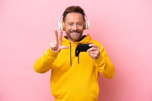 Middle age man playing with a video game controller isolated on pink background